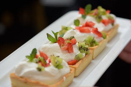 Tarts with whipped cream and strawberries and mint leaves on white plateの写真素材