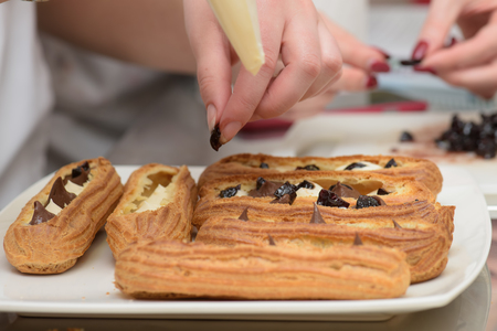 Hands decorating éclairs with custard and chocolateの写真素材