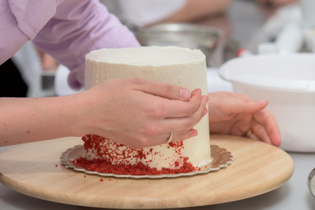 Decorating a vanilla cake with red icing sugar on a rotating plateの写真素材