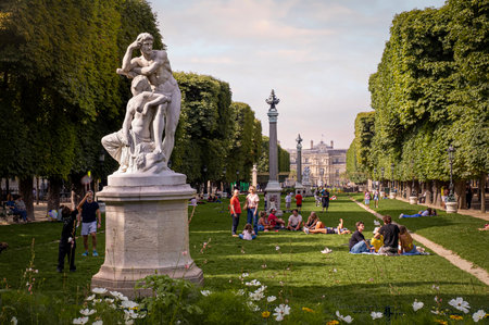 Paris, France 08 04 2023: People having rest and enjoying nice weather sitting on the grass beside The Twilight Le Crepuscule Statue at the Great Explorers Garden Jardin des Grands-Explorateurs in Parisのeditorial素材