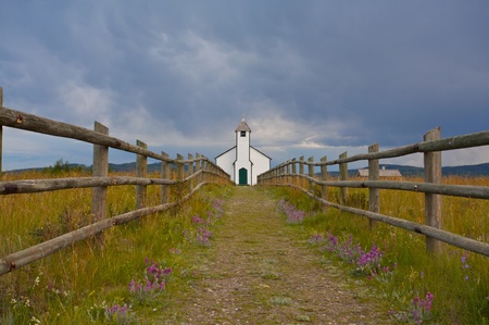 Small white country church with fence and stormy cloudsの写真素材