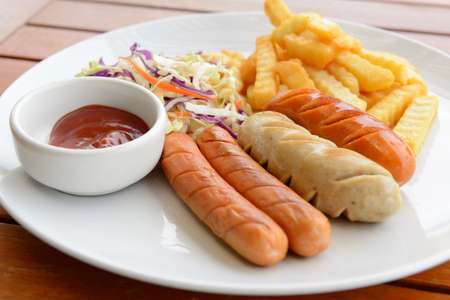 Mixed sausage served with french fried in the white dish put on the wood table の写真素材
