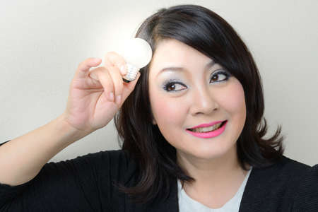 Smiling businesswoman having an idea with bright light bulb over her headの写真素材