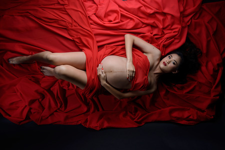 Glamour and style of beautiful young asian pregnant woman laying down on red fabric materialの写真素材