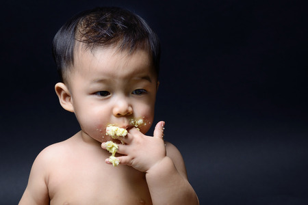 Cute asian baby eating cake with his handの写真素材