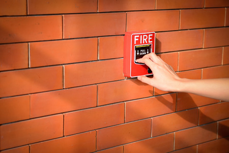 The hand of woman is pulling fire alarm on the brick wallの写真素材