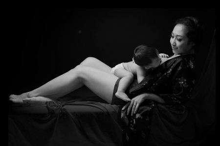 asian mother holding her laying down baby on her body and breast feeding baby in black and white colorの写真素材