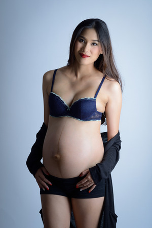 studio shot, Portrait of the young smiling pregnant long hair asian woman with braの写真素材
