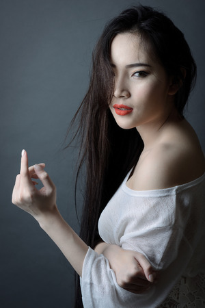 Fashion portrait of beautiful young asian woman with red lip and long black hair wearing white dressの写真素材