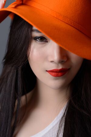 portrait close up of beautiful asian woman model in orange striped hat with red lipsの写真素材