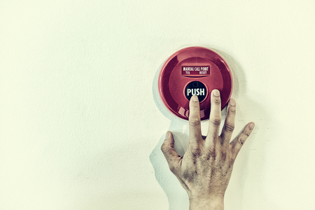 The hand of man is pushing fire alarm on the white wall in vintage colorの写真素材