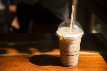 Cold coffee in plastic cup on brown wooden table at cafe.の写真素材