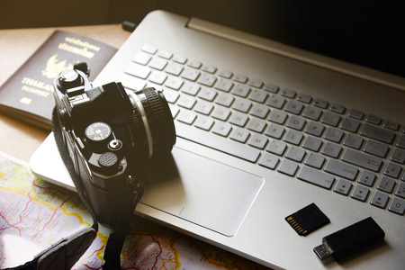 Vacation concept passport camera flash drive storage map notebook computer on wooden desk backgroundの写真素材
