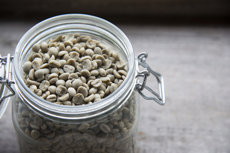 raw coffee beans,unroasted coffee beans in glass jar on wooden tableの写真素材