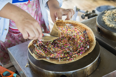 Making of crepes pancakes in open thailand street market.crepes with chocolate sauce and chopped nuts for a tasty dessert.Japanese crepes on the stoveの写真素材