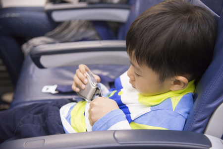 6 years old asian boy fasten seat belt with airplane onboard.safety travel with kid conceptの写真素材