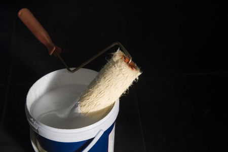 a bucket of paint and a brush roller.opened can of white paint and a roller on black background.の写真素材
