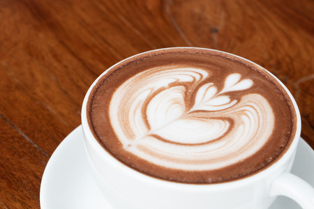coffee cup latte art on wooden table.hot drink coffee with milk froth for breakfast.heart shape art foam texture top view.の写真素材