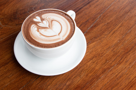 coffee cup latte art on wooden table.hot drink coffee with milk froth for breakfast.heart shape art foam texture top view.の写真素材