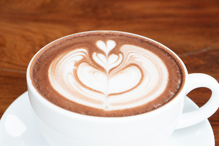 coffee cup latte art on wooden table.hot drink coffee with milk froth for breakfast.heart shape art foam texture top view.の写真素材