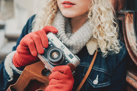 Old film camera in the hands of a young blond curly female in warm red gloves, winterの写真素材