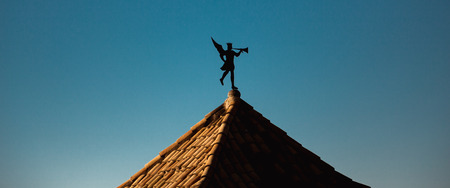 Weather vane  in the form of a trumpeting angel on a tiled roof of an ancient building in Girona, blue clear sky in backgroundの写真素材