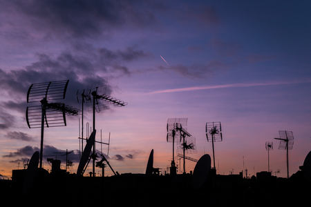 Lilac sunset and a lot of silhouettes of roofs with antennas in Barcelona. Cloudy night, the plane trace in the skyの写真素材