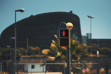 View of red traffic light for pedestrians in the form of the red man, blurred city background and teal sky, sunny summer day, Barcelona, Spain, Forum districtの写真素材