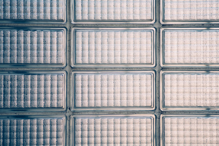 Wall composed of bluish textured glass bricks with large white seams of cracked plasterの写真素材