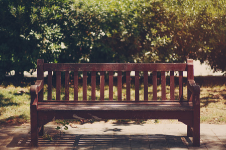 Front view of wooden maroon bench on sidewalk in Barcelona park, sunny day with bushes in backgroundの写真素材