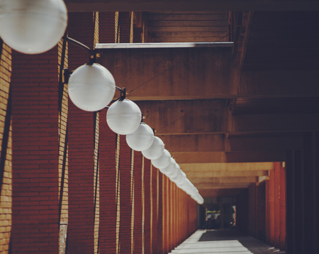 Round white ceiling lamps regularly going far into distance near brick columns of residential house, Barcelona, sunny day, Spainの写真素材