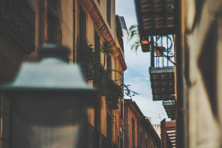 View of facades of residential houses on narrow street with sky behind with a lot of balconies, windows home plants, blurred lantern in front,  Barcelona historical district El Born, sunny summer dayの写真素材