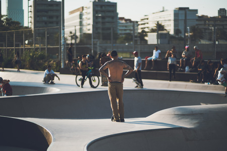 BARCELONA, SPAIN - JUNE 6, 2016: rear view of topless young man in beige trousers with a lot of tattoos watching on people in skate park, sunny summer evening, Barcelona, Spainのeditorial素材