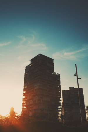 Dramatic red scenery of two residential houses with street lantern and palms in front, Barcelona district Forum, evening sky with sun flare and distant spindrift cloudsの写真素材