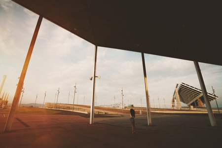 Wide angle shoot of modern contemporary asphalted area with for extreme sports, recreation and parkour in Barcelona Forum with silhouette of curly girl, huge solar station in distanceの写真素材