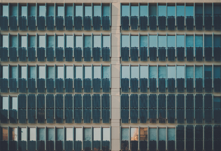 Facade of modern contemporary dark teal office building with a lot of photovoltaic plates on it,...