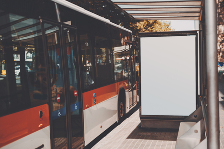White billboard with copy space area for your text message or promotional content, public information board near red bus, city bus stop with blank empty mock up banner for your advertisingの写真素材