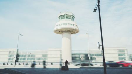 Rear view of tired man with luggage waiting for taxi after his arrival in Barcelona, silhouette of young guy with several suitcases in front of air traffic control tower of modern contemporary airportの写真素材