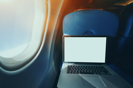 Wide angle shooting of contemporary laptop with blank screen on the blue table of airplane seat, mock up of modern portable computer next to illuminator of flying plane with sunny day outsideの写真素材