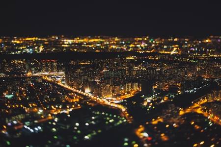 True tilt shift shooting of residential district of night metropolis from very high above: multiple residential houses and orange lights from windows, strong bokeh in background and foregroundの写真素材