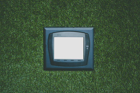 Modern multifunctional climate control device with white blank screen on artificial grass wall, mock up of remote control unit on office green wall to operate different devices in recreational zoneの写真素材