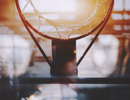 View from bottom of basketball hoop and basket with a lot of abstract reflections and aberrations around on summer sunny day with blurred beams of modern contemporary office stadium in backgroundの写真素材