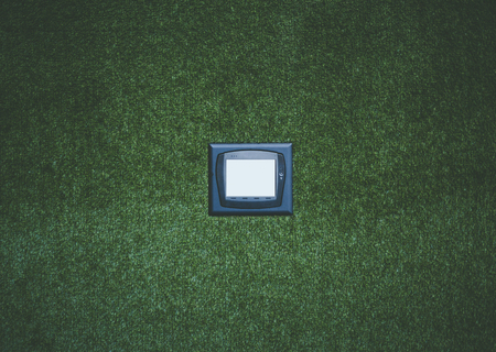 Modern multifunctional climate control device with white blank screen on artificial grass wall, mock up of remote control unit on office green wall to operate different devices in recreational zoneの写真素材