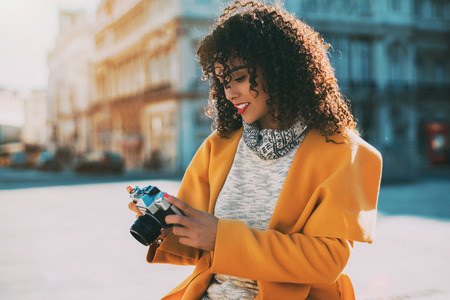 Attractive curly Brazilian woman with vintage camera on street of Lisbon, adult white stylish lady...