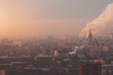Close-up shooting from high point of metropolitan city: residential buildings illuminated by morning sun, Government building, smoke from fuming chimneys in distance polluting environmentの写真素材