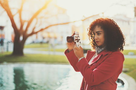 Serious pensive beautiful adult curly professional photographer in red trendy coat making photos...