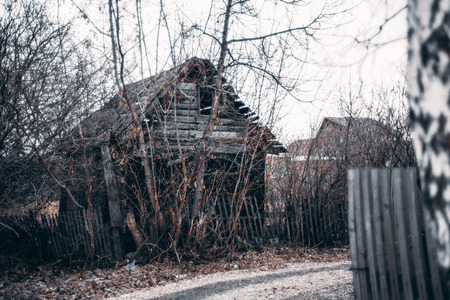 Abandoned old summer house with fallen fence on street of suburban village on springtime or autumn with dry leaves on the ground and bare treesの写真素材
