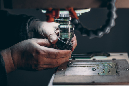 View of worker hands while he is changing drilling tool cutter in CNC milling machine during pause of treatment of aluminum blank fixed on moving table in dark settings of workshop roomの写真素材