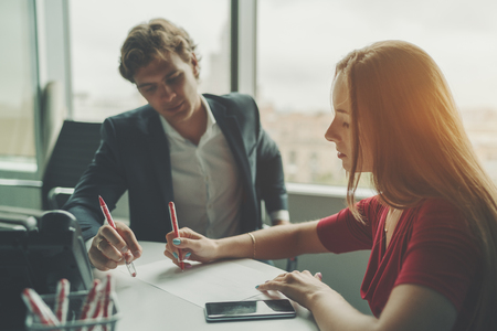 Attractive man entrepreneur having work conversation with his female beautiful co-worker, businesswoman explaining her colleague  new development strategy using sheet of paper and pen during meetingの写真素材