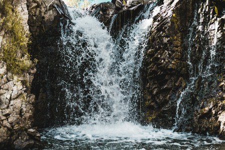 View of beautiful low wild waterfall in mossy cliffs: two streams of water go into one during falling down into foam, Russia, Altai mountainsの写真素材